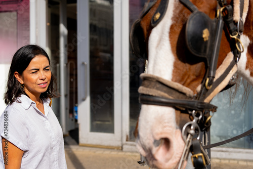 Latin woman trying to pet beautiful horse used to carry float in the city center for tourist