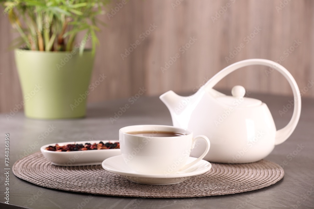 Aromatic tea in cup, saucer, teapot and dry flower petals on grey table Aromatic tea in cup, saucer, teapot and dry flower petals on grey table