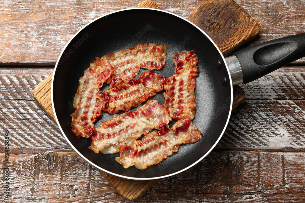 Delicious bacon slices in frying pan on wooden table, top view