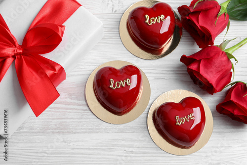St. Valentine's Day. Delicious heart shaped cakes, roses and gift on white wooden table, flat lay