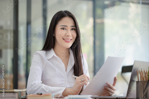 Happy asian young businesswoman holding documents folders in office working space, Asian female employee using laptop talking on the phone at workplace. © SOMKID