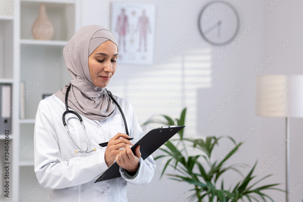 A dedicated female Muslim doctor in a hijab and white coat is focused on patients' reports while working in a clinic. A dedicated female Muslim doctor in a hijab and white coat is focused on patients' reports while working in a clinic.