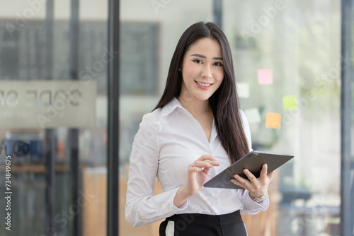 Happy asian young businesswoman using digital tablet standing in office office working space.