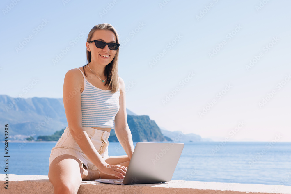 Freedom of movement. Workplace by the sea. A smiling woman works on a laptop in the summer by the sea