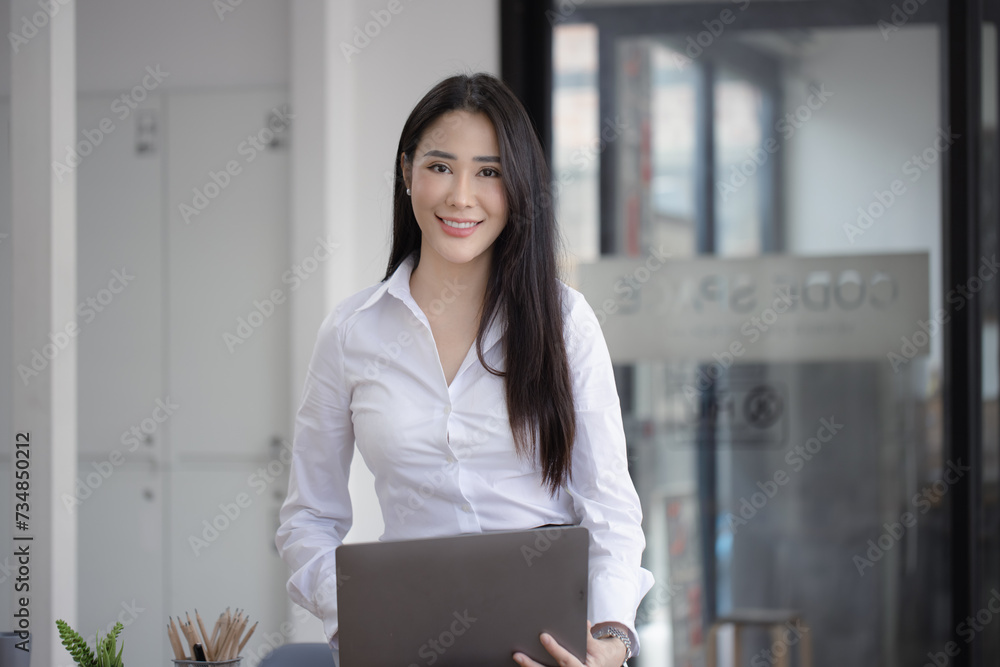 Happy asian young businesswoman using laptop with documents in office working space. Happy asian young businesswoman using laptop with documents in office working space.