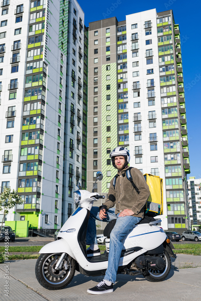 Food delivery service. A courier with a yellow bag on a scooter against the background of an urban area Food delivery service. A courier with a yellow bag on a scooter against the background of an urban area