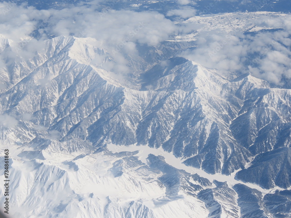 Fototapeta premium 飛行機で雲の上から見た雪で白くなった山