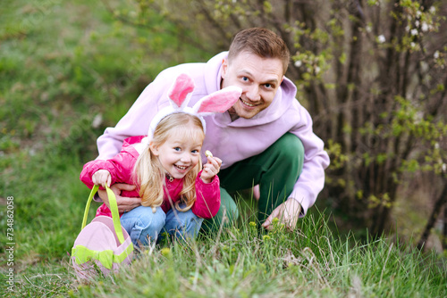 Canvastavla Caucasian father and daughter with bunny ears collecting Easter eggs and putting Easter eggs in baskets in the park