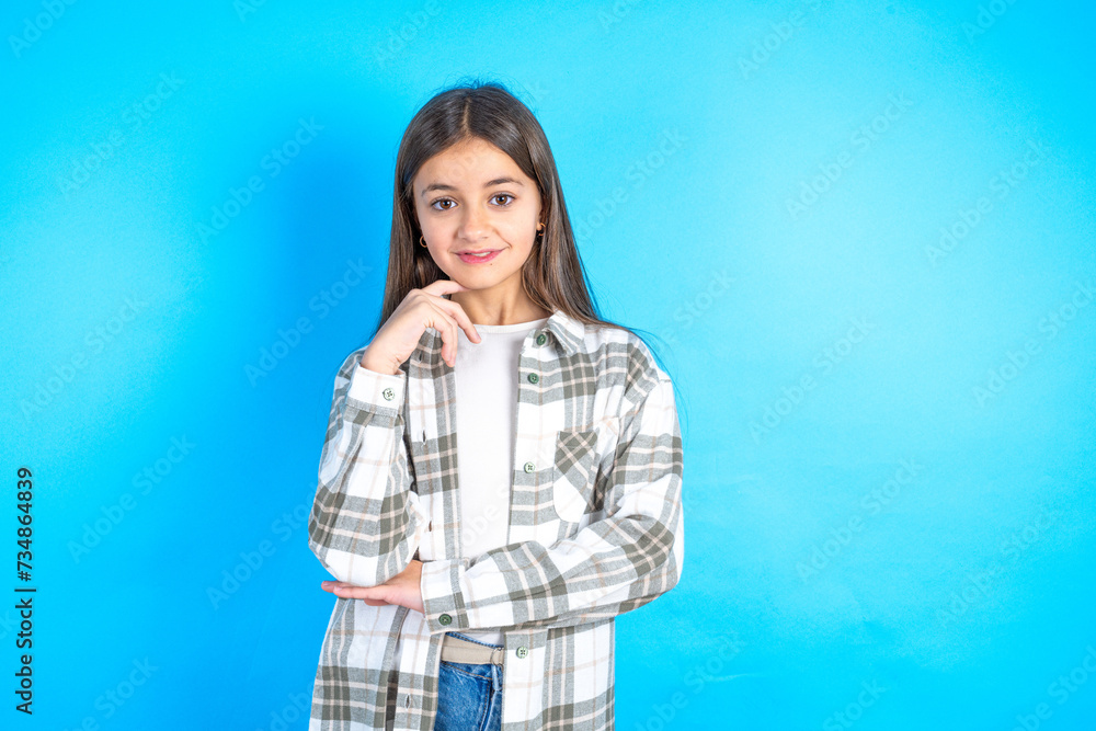 Optimistic Young beautiful teen girl wearing check shirt keeps hands partly crossed and hand under chin, looks at camera with pleasure. Optimistic Young beautiful teen girl wearing check shirt keeps hands partly crossed and hand under chin, looks at camera with pleasure.