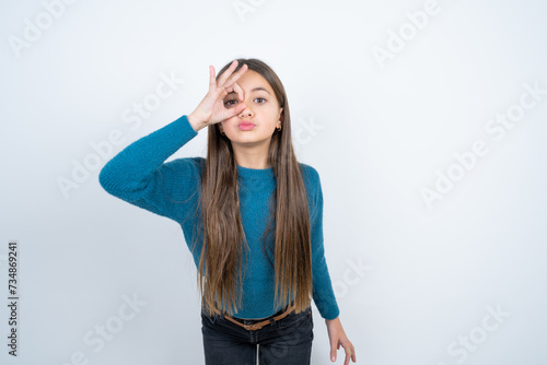 Young beautiful teen girl wearing blue T-shirt doing ok gesture shocked with surprised face, eye looking through fingers. Unbelieving expression.