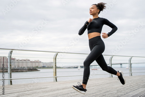 Fit woman in sportswear jogging along a wooden pier by the waterfront, focused on her workout