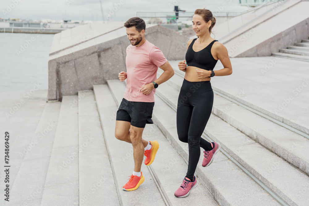 Active couple jogging up the stairs by the sea, showcasing healthy lifestyle and partnership in fitness with a serene waterfront backdrop. Active couple jogging up the stairs by the sea, showcasing healthy lifestyle and partnership in fitness with a serene waterfront backdrop.