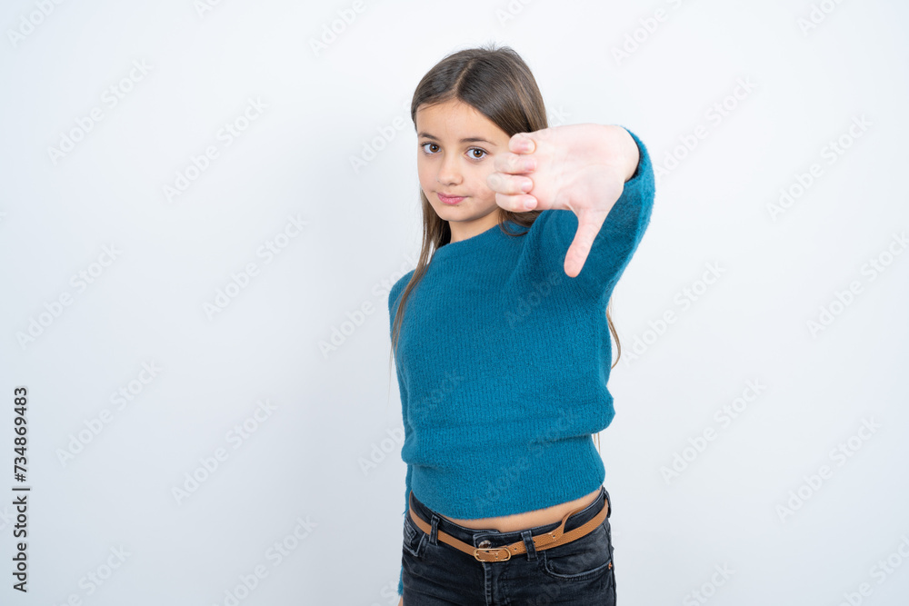 Young beautiful teen girl wearing blue T-shirt feeling angry, annoyed, disappointed or displeased, showing thumbs down with a serious look Young beautiful teen girl wearing blue T-shirt feeling angry, annoyed, disappointed or displeased, showing thumbs down with a serious look
