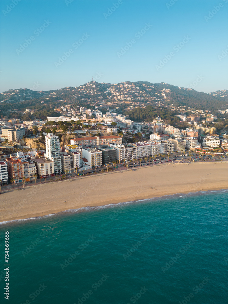 Aerial view of Lloret del Mar City. Mediterranean coastal town in Catalonia, Spain. One of the most popular Costa Brava beaches. Famous travel destination. Vertical photo. Sunset warm colours