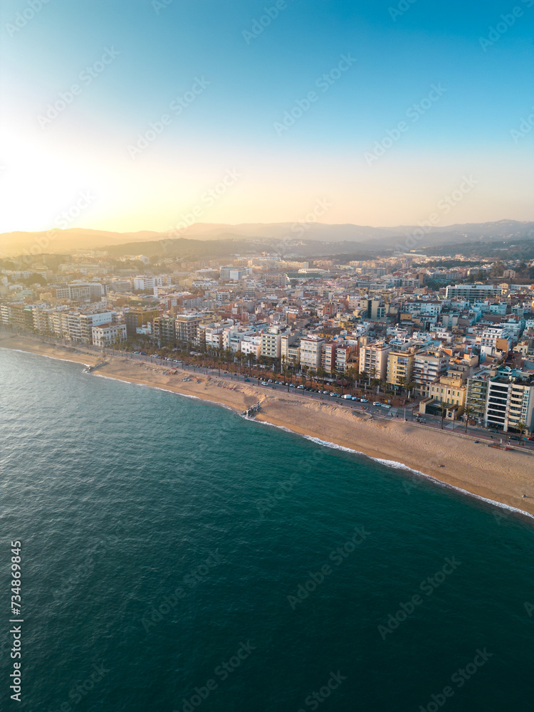 Fototapeta premium Aerial view of Lloret del Mar City. Mediterranean coastal town in Catalonia, Spain. One of the most popular Costa Brava beaches. Famous travel destination. Vertical photo. Sunset warm colours