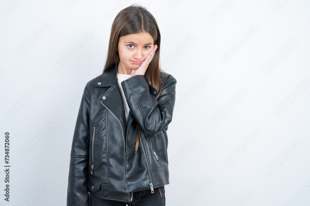 Sad lonely Young beautiful teen girl wearing biker jacket touches cheek with hand bites lower lip and gazes with displeasure. Bad emotions Sad lonely Young beautiful teen girl wearing biker jacket touches cheek with hand bites lower lip and gazes with displeasure. Bad emotions