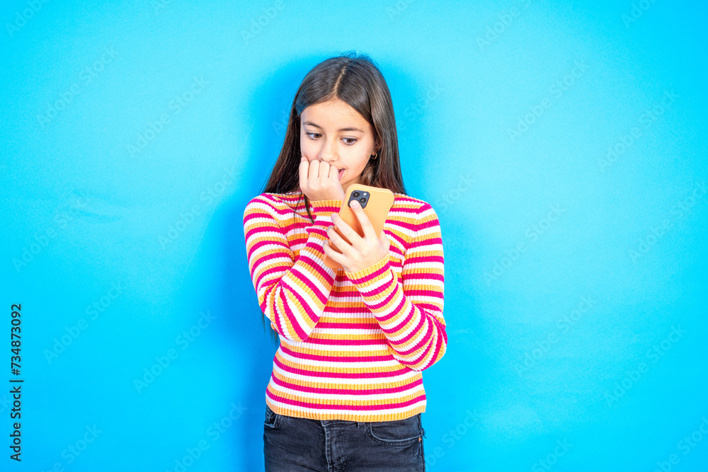 Afraid funny Young kid girl wearing striped t-shirt holding telephone and bitting nails Afraid funny Young kid girl wearing striped t-shirt holding telephone and bitting nails