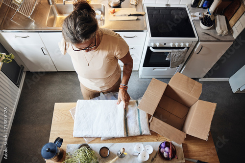 High angle view of woman with disability opening package while standing in kitchen at home photo