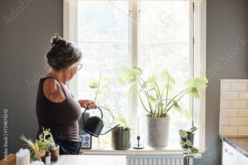 Mature woman with disability watering plants on window sill at home photo