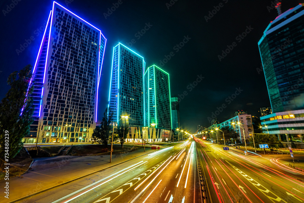 Fototapeta premium Neon light on modern skyscrapers and avenue traffic in Kyiv