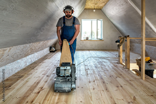 Professional worker carpenter grinding sanding a wooden floor by using floor sander. Industrial theme