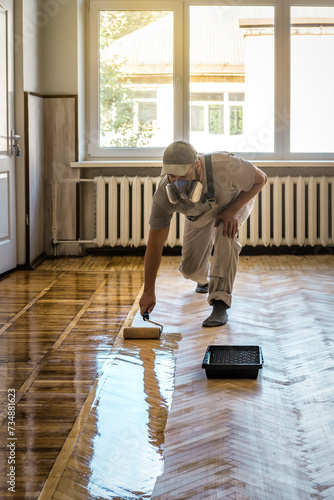 Renovation of old parquet floor, Worker varnishing wooden floor by roller