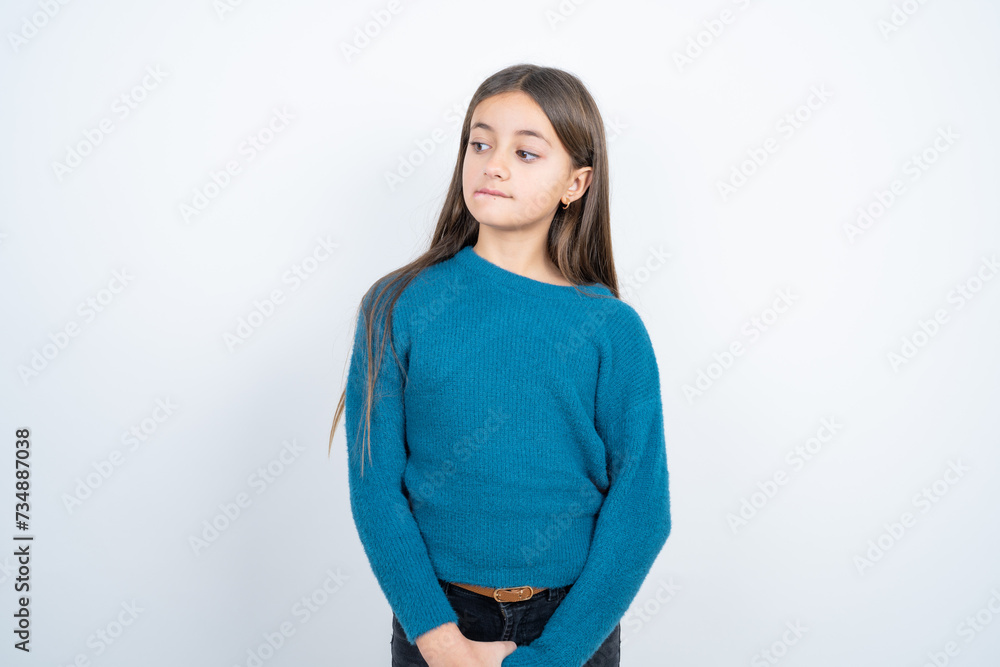 Amazed beautiful kid girl wearing blue sweater bitting lip and looking tricky to empty space. Amazed beautiful kid girl wearing blue sweater bitting lip and looking tricky to empty space.