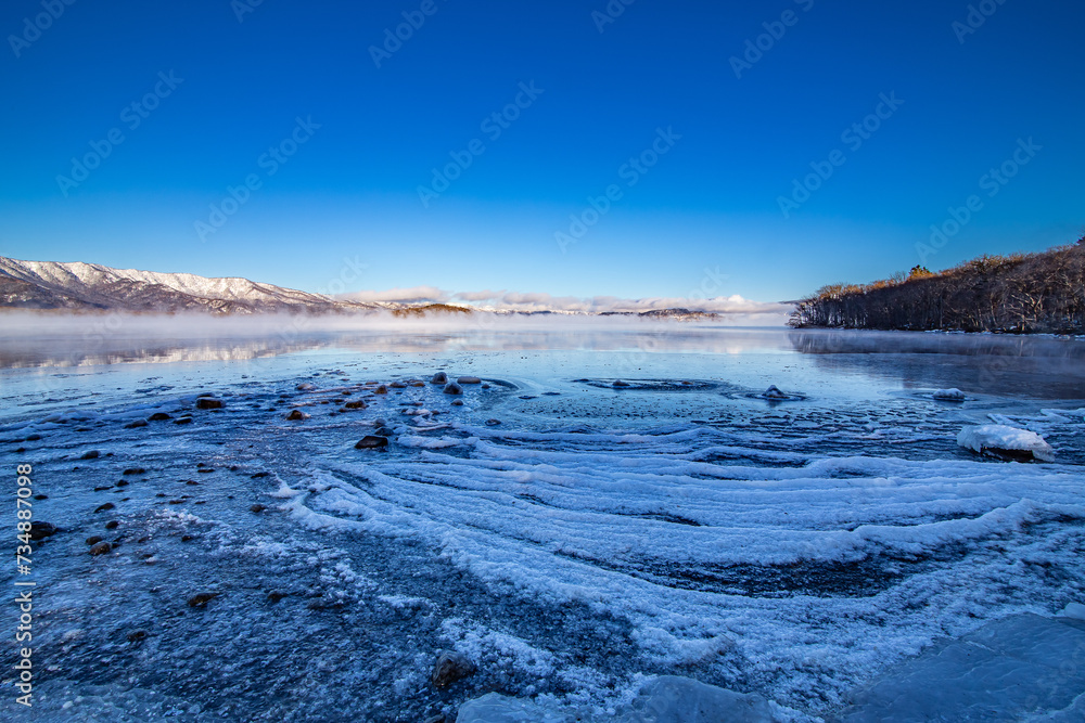 Obraz premium 波のようなテクスチャの氷に覆われた湖の岸辺。日本の北海道の屈斜路湖の冬。北国の冬の風変わりな自然の現象。