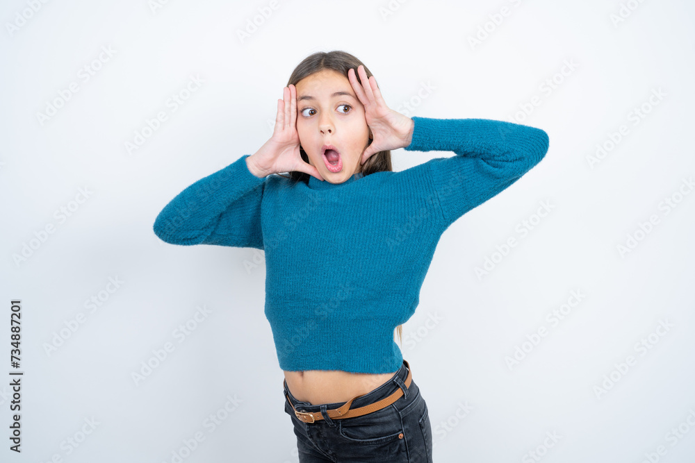 beautiful kid girl wearing blue sweater with scared expression, keeps hands on head, jaw dropped, has terrific expression. Omg concept beautiful kid girl wearing blue sweater with scared expression, keeps hands on head, jaw dropped, has terrific expression. Omg concept