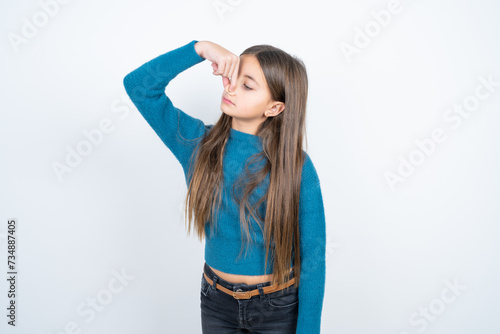 beautiful kid girl wearing blue sweater smelling something stinky and disgusting, intolerable smell, holding breath with fingers on nose. Bad smell © Roquillo