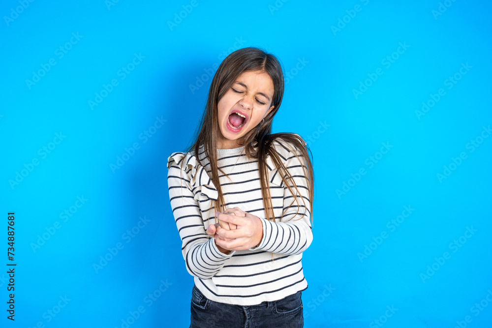 Beautiful kid girl wearing striped T-shirt Suffering pain on hands and fingers, arthritis inflammation Beautiful kid girl wearing striped T-shirt Suffering pain on hands and fingers, arthritis inflammation