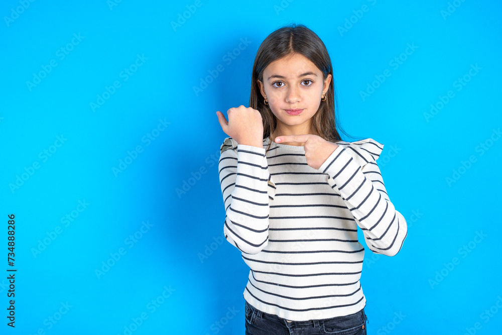Fototapeta premium beautiful kid girl wearing plaid shirt In hurry pointing to wrist watch, impatience, looking at the camera with relaxed expression