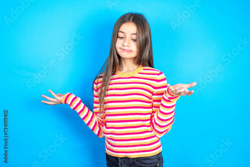 Photos Careless attractive beautiful kid girl wearing  striped T-shirt shrugging shoulders, oops
