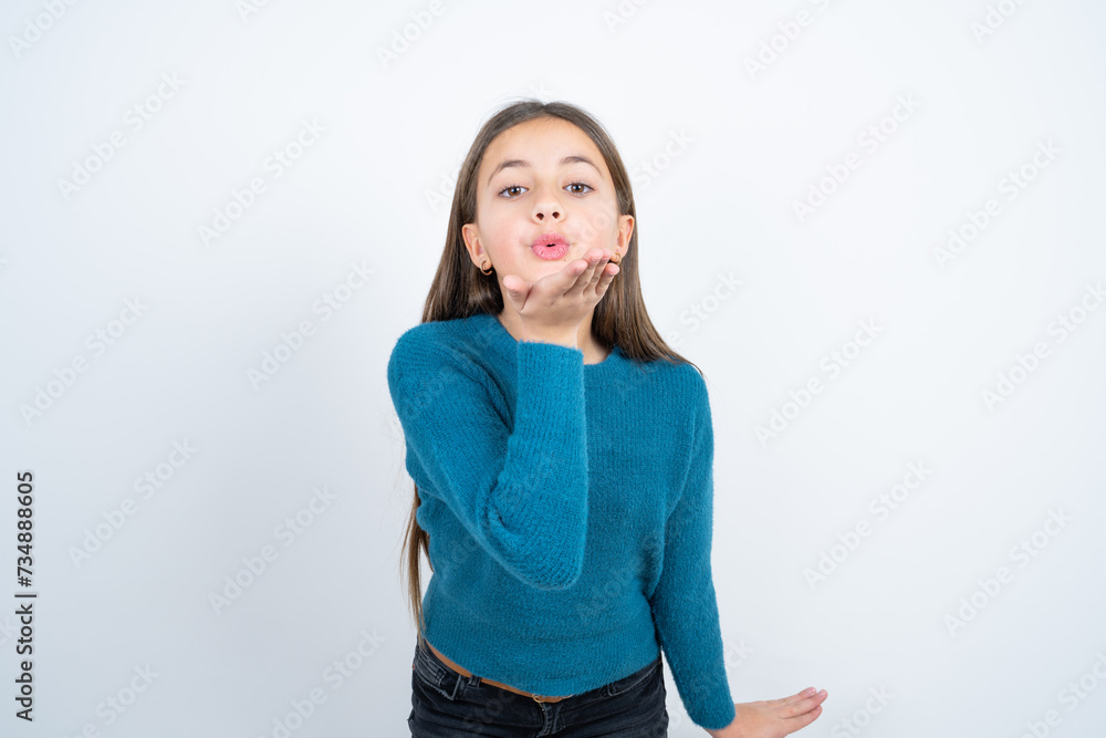beautiful kid girl wearing blue sweater looking at the camera blowing a kiss with hand on air being lovely and sexy. Love expression. beautiful kid girl wearing blue sweater looking at the camera blowing a kiss with hand on air being lovely and sexy. Love expression.