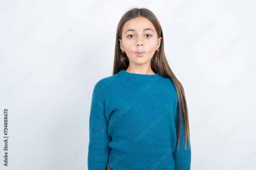 Shot of pleasant looking beautiful kid girl wearing blue sweater , pouts lips, looks at camera, Human facial expressions Shot of pleasant looking beautiful kid girl wearing blue sweater , pouts lips, looks at camera, Human facial expressions