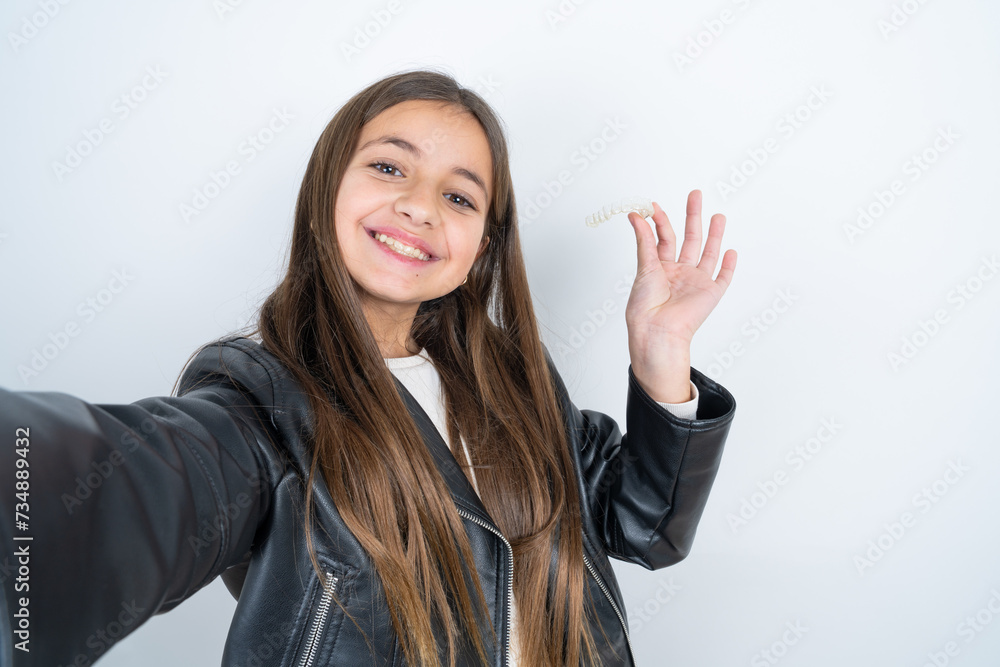 Young beautiful teen girl wearing biker jacket make selfie holding an invisible braces aligner, recommending this new treatment. Dental healthcare concept. Young beautiful teen girl wearing biker jacket make selfie holding an invisible braces aligner, recommending this new treatment. Dental healthcare concept.