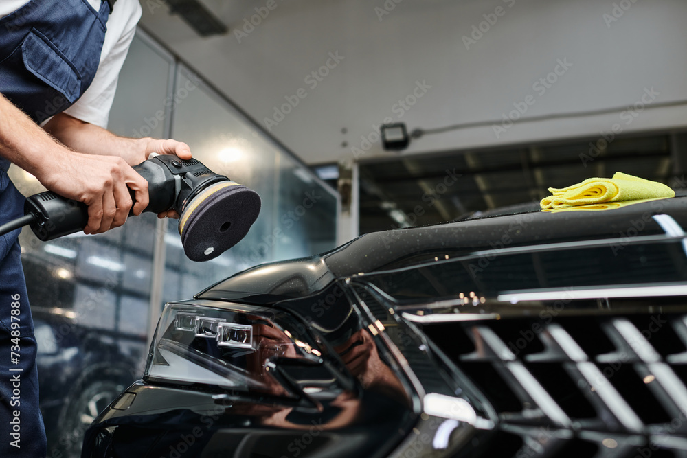 cropped view of professional hard working specialist using polishing machine on black modern car
