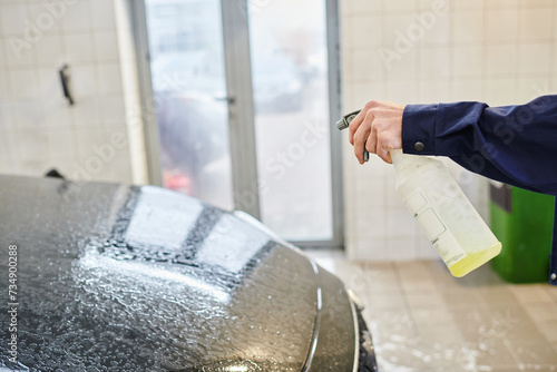 cropped view of enthusiastic professional worker in uniform using pulverizer with water to clean car photo