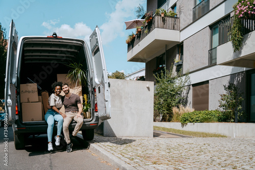 Multiracial couple sitting in van trunk near building photo