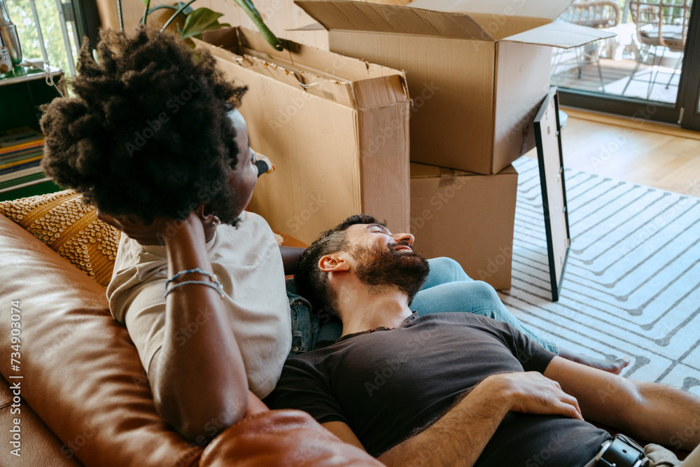 © Maskot - Multiracial couple relaxing together on sofa in living room at new home