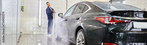 appealing devoted specialist in comfy blue uniform using hose to wash black modern car, banner