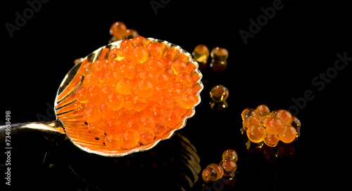 Red Caviar in a spoon isolated on black background. Close-up of salmon fish roe caviar. Delicatessen. Texture of trout caviar. Seafood backdrop 