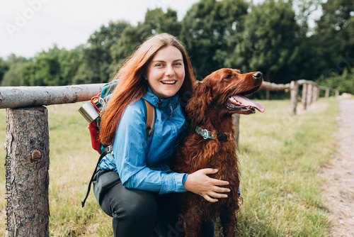 Happy 30s Girl loving and hugging tightly her dog. Travel and hiking with pet. Redhead Woman in active trekking clothes with dog having a halt after hiking, irish setter