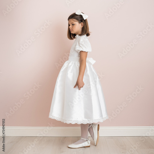 brunette girl 9 years old in a white festive dress on a pale pink background, dress for a wedding, first communion, birthday, celebration