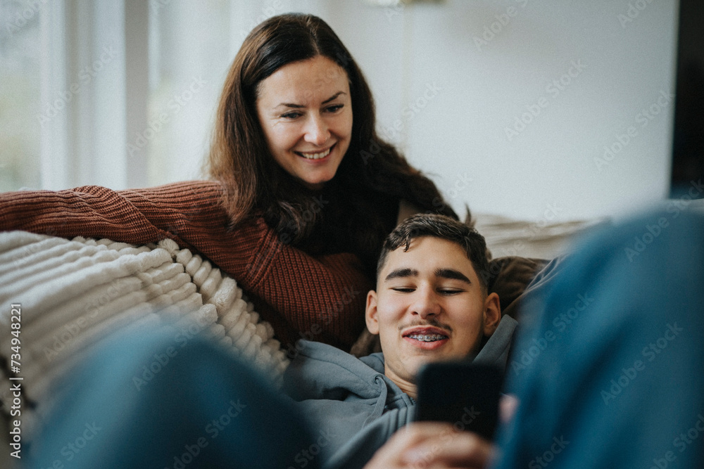 Smiling boy sharing smart phone with mother while lying on sofa in living room at home Smiling boy sharing smart phone with mother while lying on sofa in living room at home