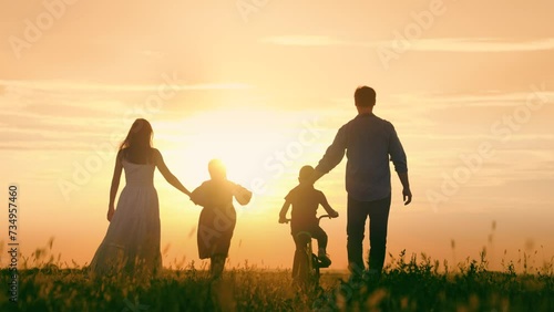 Family walk, mom dad, child, parental support. Dad, Mom teaches children to ride bike, sunset. Childhood dream of riding bike. Father teaches his child to keep balance while sitting on bicycle. Kids photo