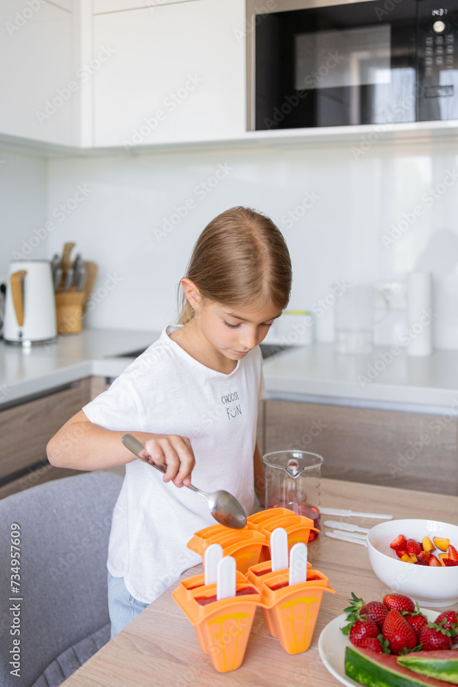 The process of making ice cream. Child making tasty ice lollipops in moulds on countertop in kitchen during free time.