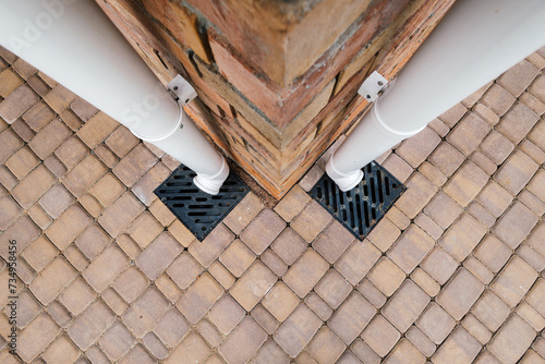 Bottom of red brick wall with two metal downspout and pit.