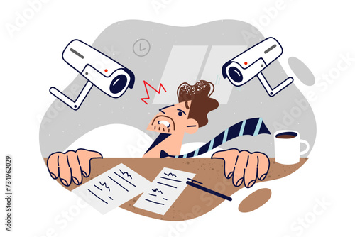 Business man suffers from persecution mania, hiding under table due to surveillance cameras
