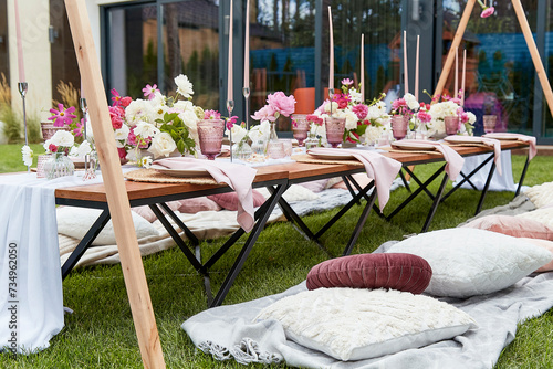 Pink girle aesthetic picnic table setting with pink flowers bouquets, cozy pillows, candles decor outdoor